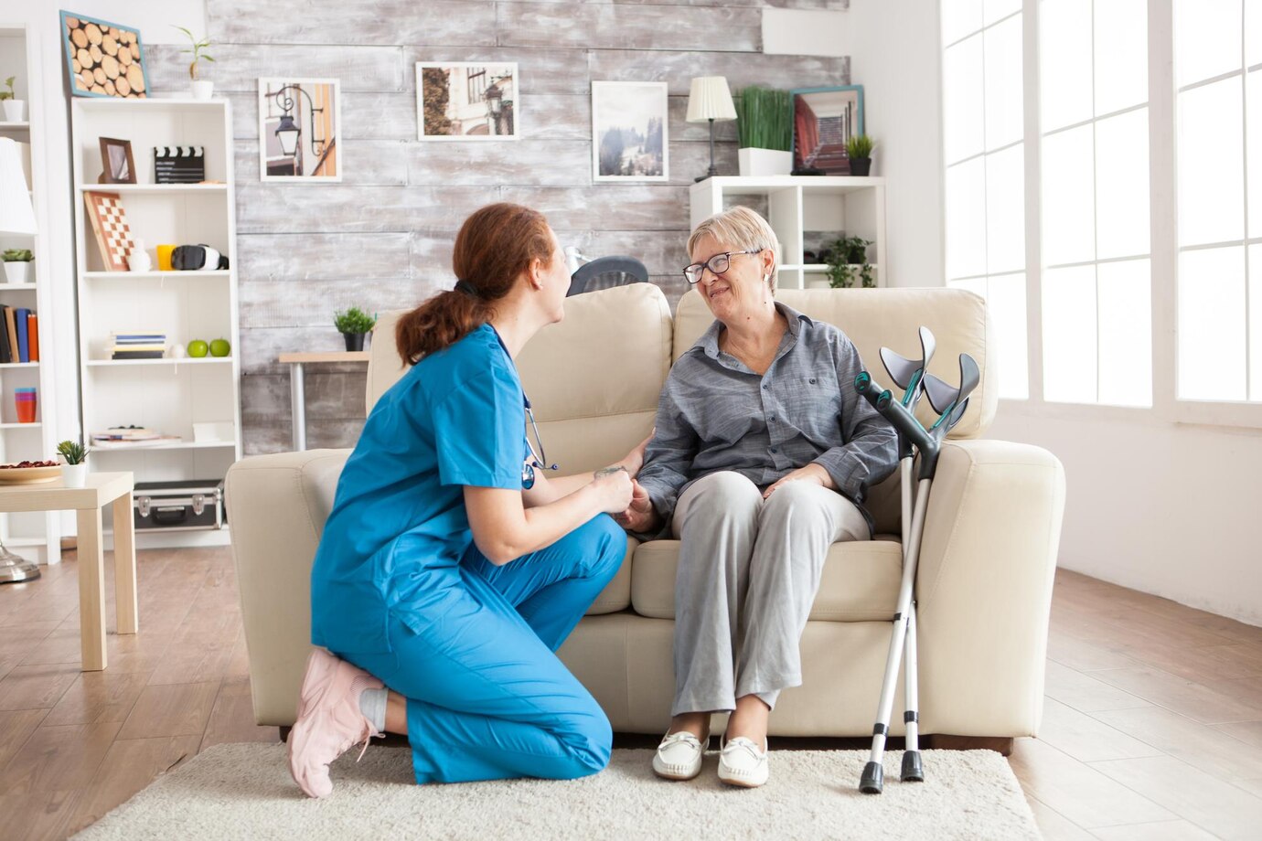 happy-old-woman-nursing-home-sitting-couch-talking-with-her-caretaker-retired-woman-with-crutches_482257-45102